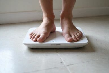 A person weighing themselves on a scale with a thoughtful expression